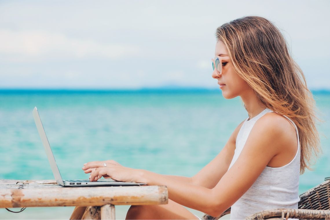 Digital nomad works on laptop from beach