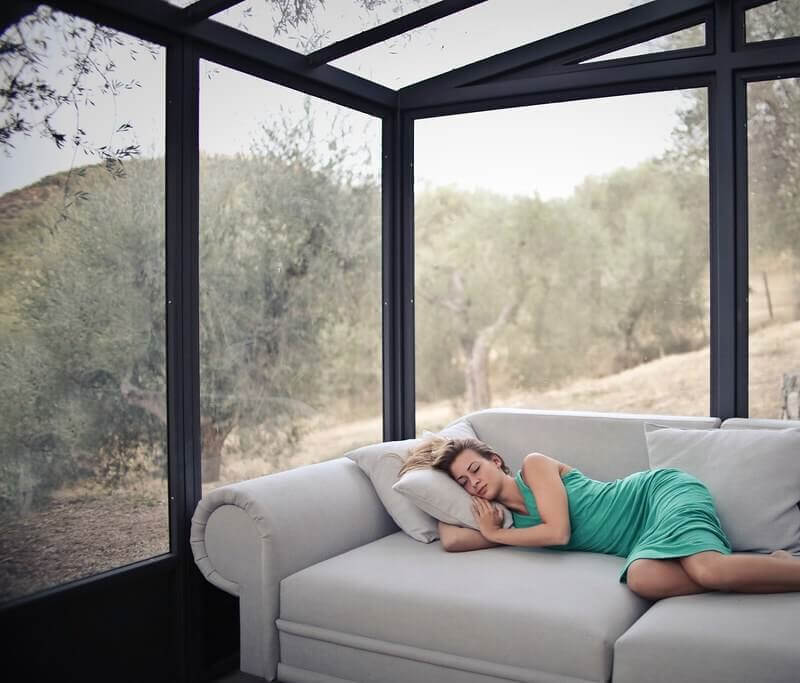 Woman asleep on sofa in glass walled conservatory